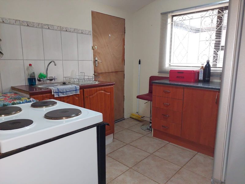 A functional kitchen featuring wood-finish cabinetry, tiled backsplash, and tiled flooring, providing a practical layout with an integrated stove and sink area.