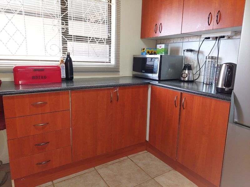 A functional kitchen featuring wood-look laminate cabinetry, dark laminate countertops, tiled flooring, and a window with security bars and venetian blinds.