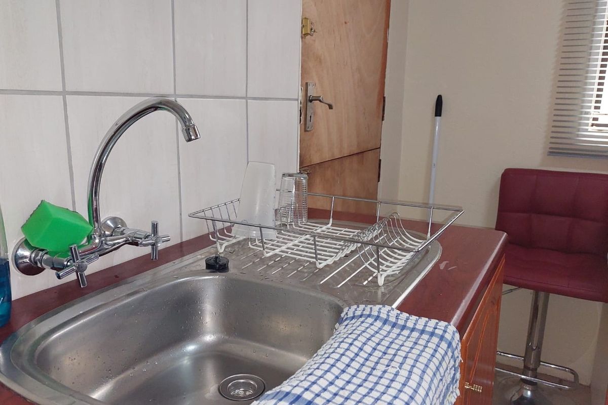 A functional kitchen area featuring a stainless steel sink, chrome mixer tap, tiled splashback, and laminate countertops with wooden cabinetry.
