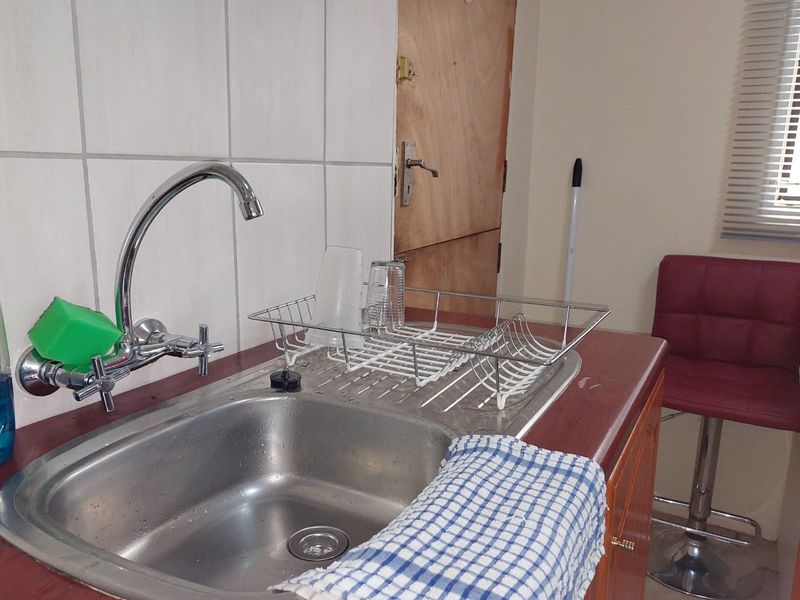A functional kitchen area featuring a stainless steel sink, chrome mixer tap, tiled splashback, and laminate countertops with wooden cabinetry.