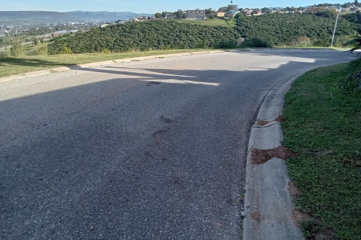 A view of the asphalt street and concrete curbing bordering the vacant residential land, featuring a scenic hillside backdrop.
