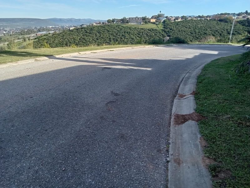 A view of the asphalt street and concrete curbing bordering the vacant residential land, featuring a scenic hillside backdrop.