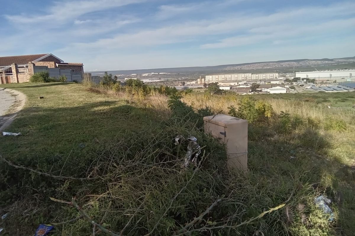 A view of the vacant residential land featuring natural vegetation and a utility box, overlooking a distant industrial area.