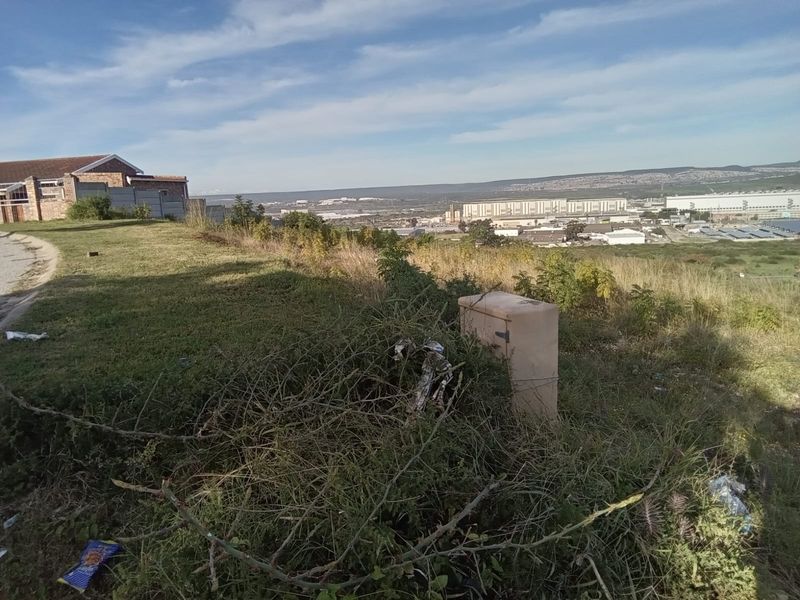 A view of the vacant residential land featuring natural vegetation and a utility box, overlooking a distant industrial area.
