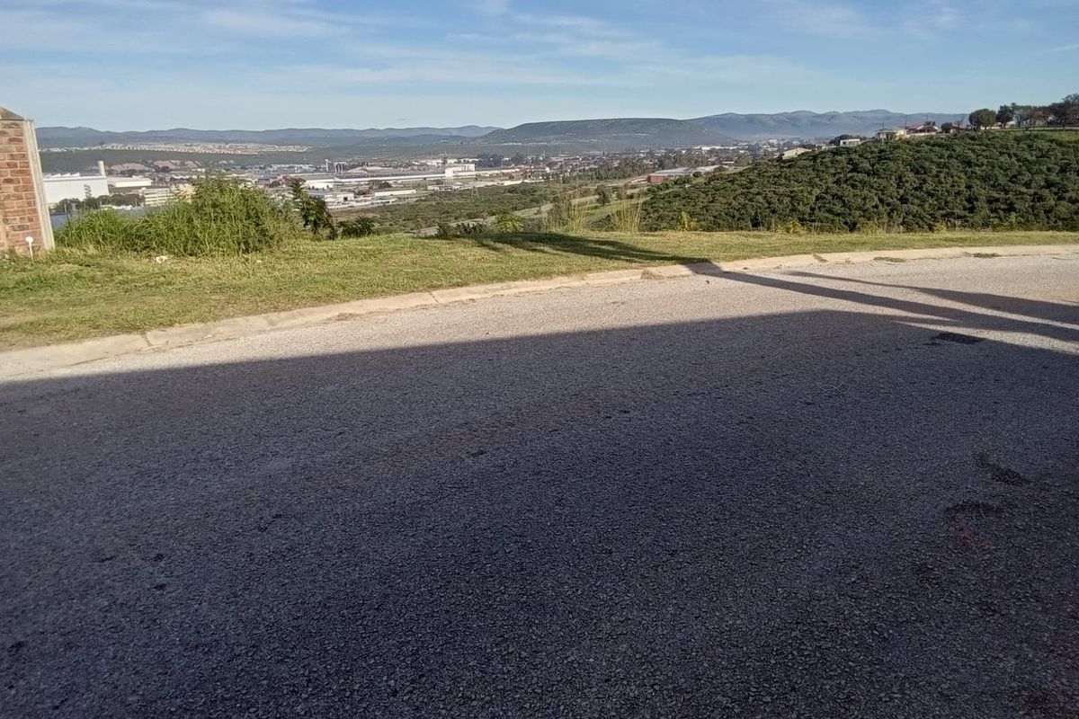 A scenic elevated view overlooking the surrounding landscape and industrial area, captured from the edge of a paved residential street.