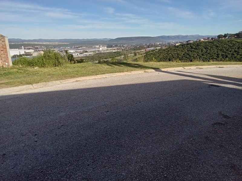 A scenic elevated view overlooking the surrounding landscape and industrial area, captured from the edge of a paved residential street.