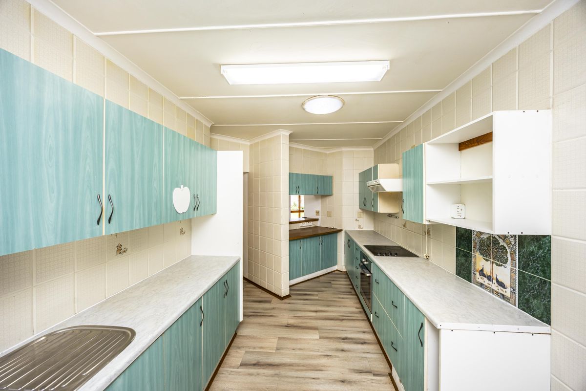 A galley-style kitchen featuring dated cabinetry, laminate countertops, built-in oven and hob, and tiled splashbacks, offering a functional layout ready for modernization.