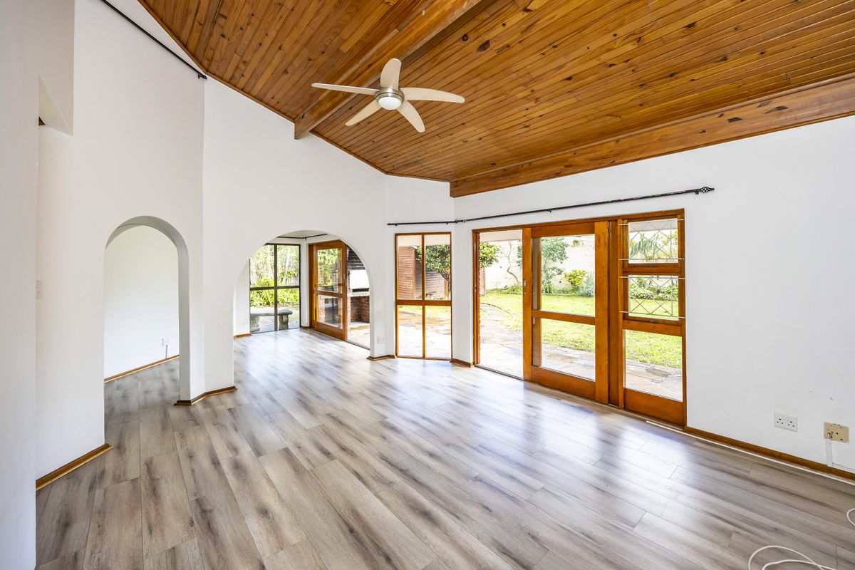 Spacious living area featuring a vaulted timber ceiling, laminate flooring, and large timber-framed doors providing direct access to the garden.