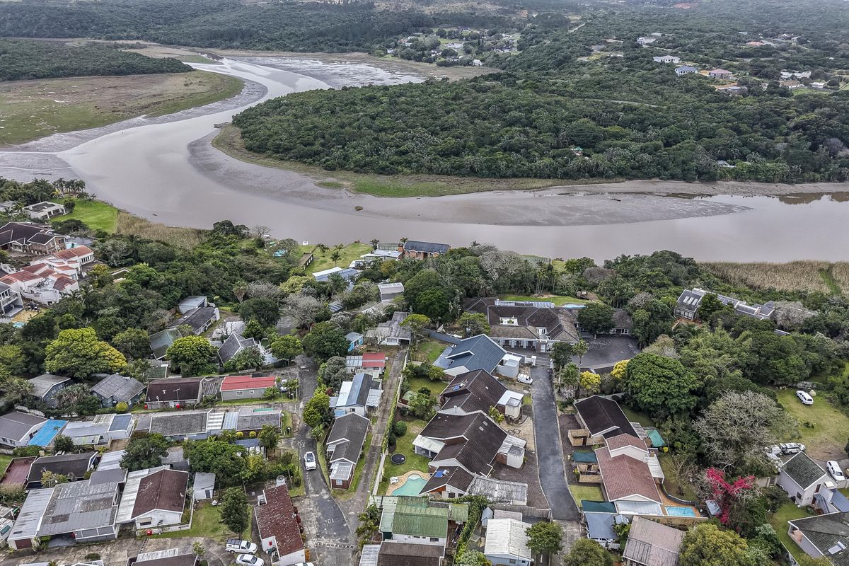 An aerial view of a residential cluster development situated near a river, showcasing the surrounding landscape and property layout.