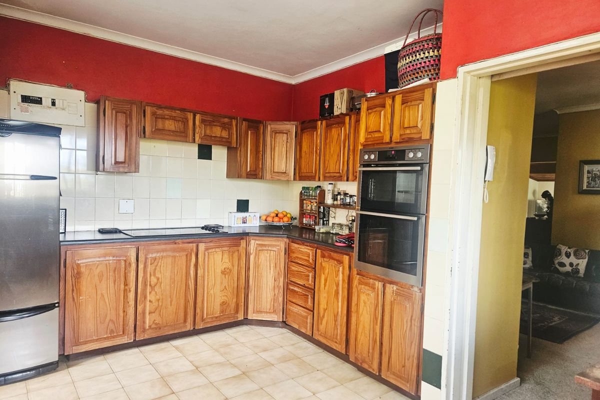 A functional kitchen featuring wooden cabinetry, a built-in double oven, electric hob, and tiled splashback, offering a traditional layout with potential for modernization.