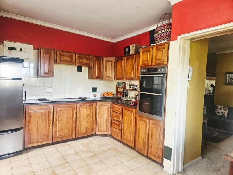 A functional kitchen featuring wooden cabinetry, a built-in double oven, electric hob, and tiled splashback, offering a traditional layout with potential for modernization.