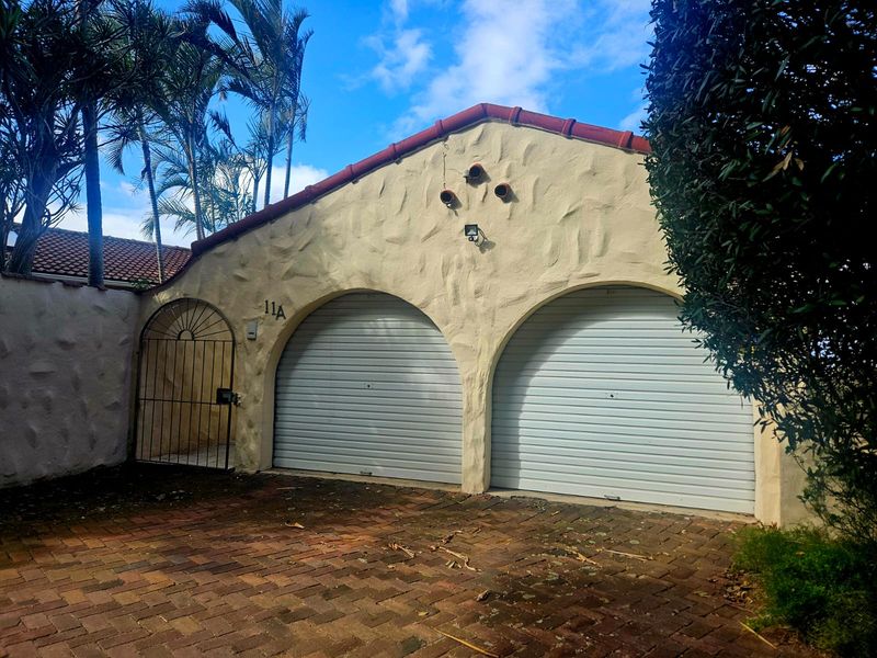 Exterior view of a double garage featuring arched openings, roller doors, and a brick-paved driveway with an adjacent pedestrian gate.