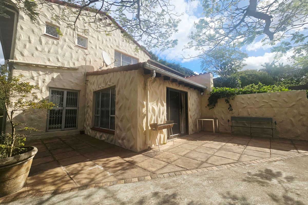 Rear exterior view of the house featuring a textured stone facade, a paved patio area, and security bars on the windows.