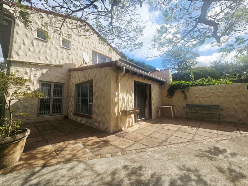 Rear exterior view of the house featuring a textured stone facade, a paved patio area, and security bars on the windows.