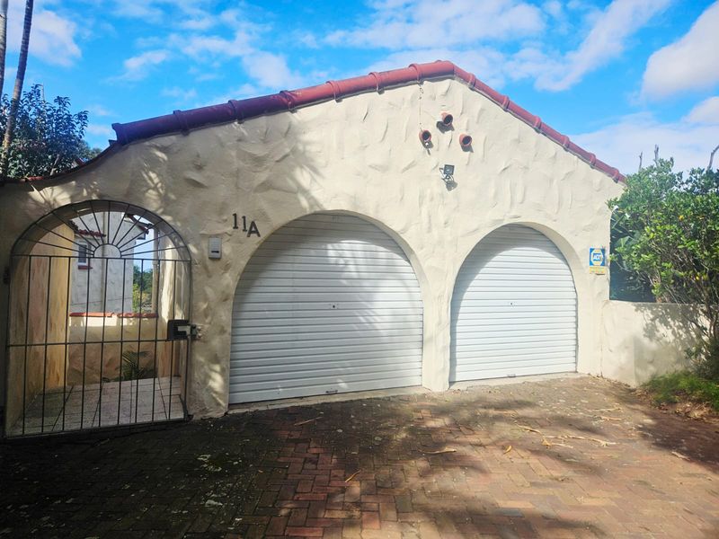 A double garage featuring arched roller doors, a textured stucco facade, and a secure wrought iron pedestrian gate entrance.