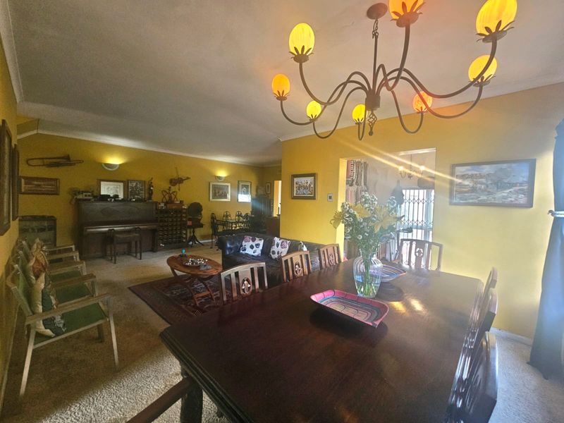 Spacious open-plan living and dining area featuring warm yellow walls, a decorative chandelier, and wall sconces, offering a traditional and inviting atmosphere.