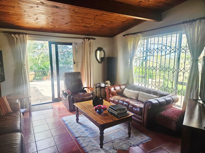 A living room featuring a warm timber-clad ceiling with exposed beams, ceramic tiled flooring, and large sliding glass doors leading to an outdoor patio area.