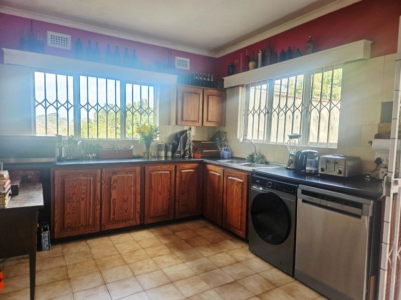 A functional kitchen featuring wooden cabinetry, laminate countertops, tiled flooring, and security bars on the windows.
