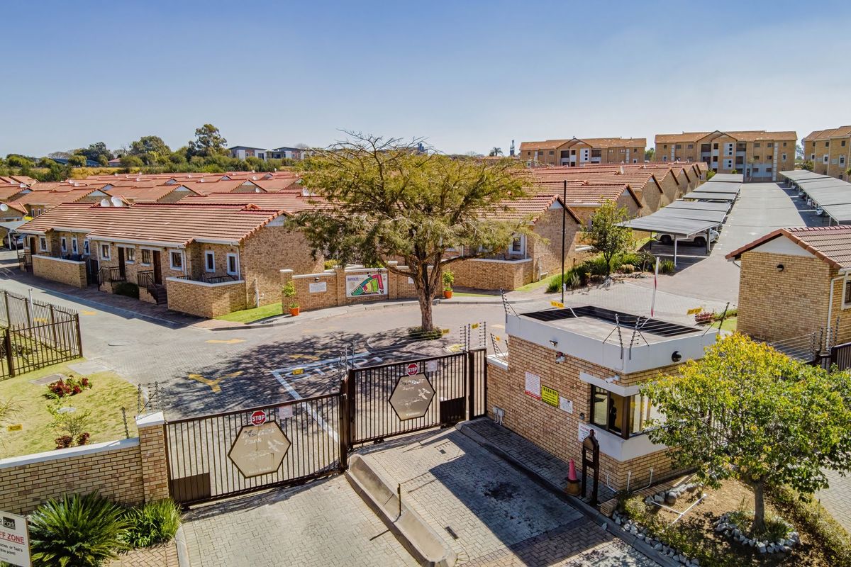 Aerial view of a secure residential apartment complex featuring a gated entrance, guard house, paved driveways, and covered parking bays.