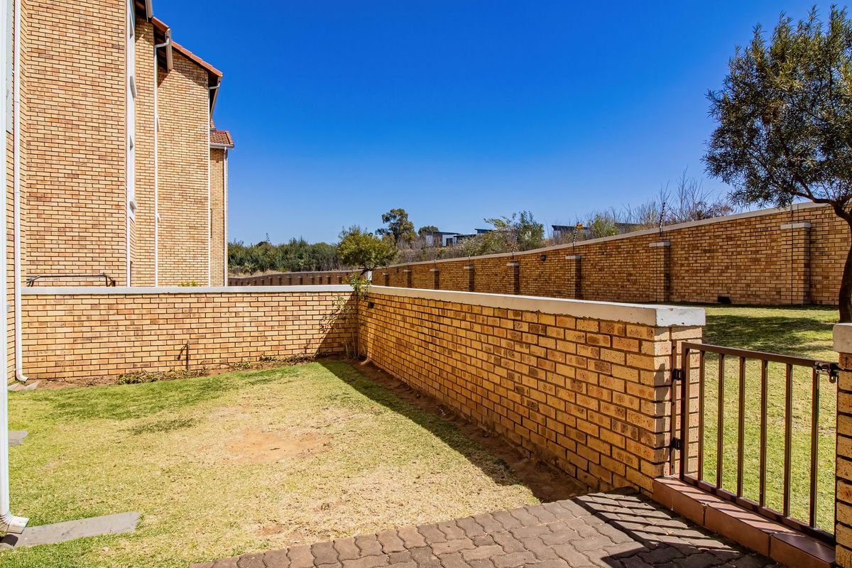 A private rear garden area featuring a brick boundary wall, a small lawn, and a paved patio section.