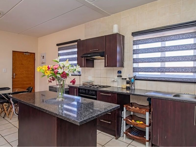 Open plan kitchen featuring dark wood cabinetry, granite countertops, built-in oven and hob, and tiled flooring, seamlessly connecting to the dining area.
