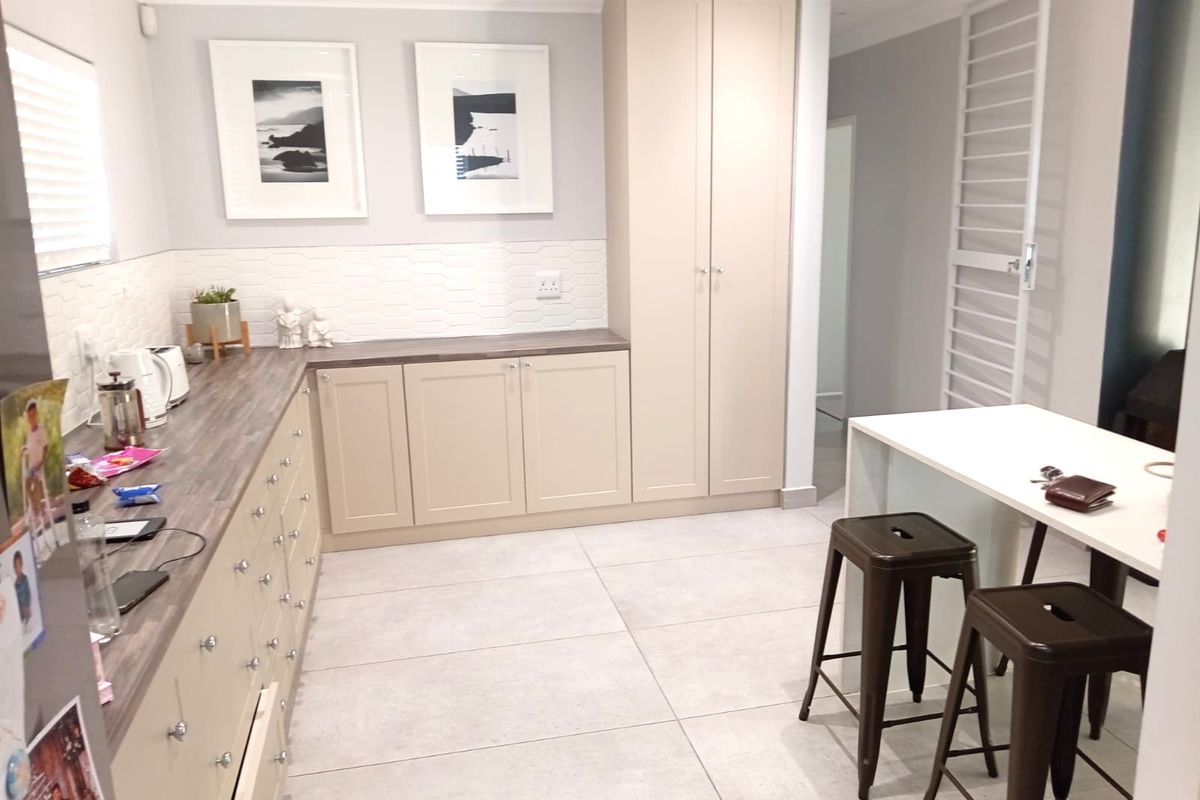 Modern kitchen featuring neutral-toned built-in cabinetry, wood-look laminate countertops, a textured tiled backsplash, and large-format porcelain floor tiles.