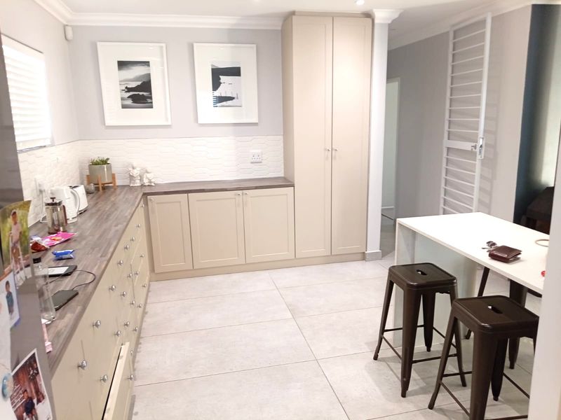 Modern kitchen featuring neutral-toned built-in cabinetry, wood-look laminate countertops, a textured tiled backsplash, and large-format porcelain floor tiles.