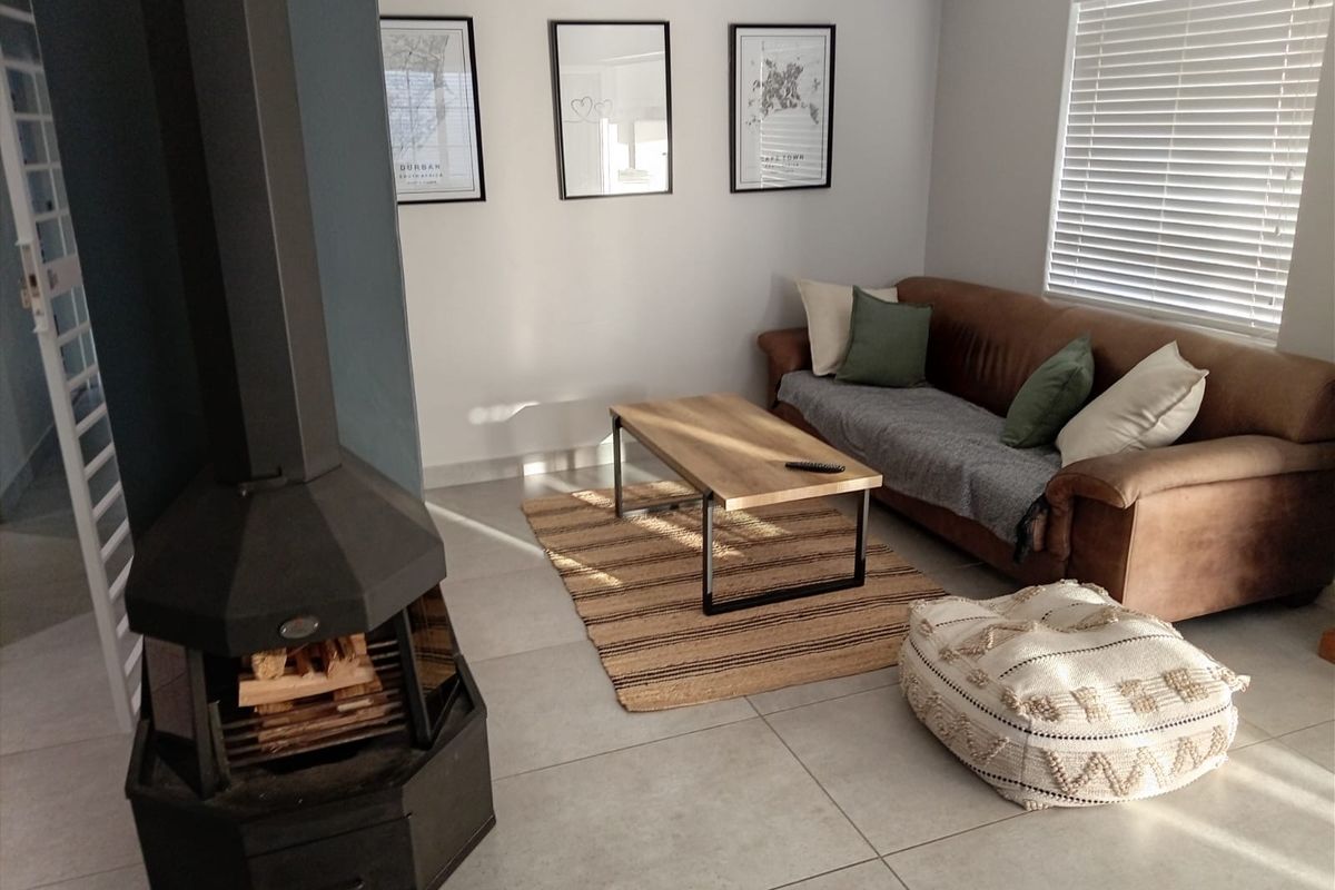 A bright living room featuring large format floor tiles, a modern freestanding fireplace, and venetian blinds, creating a comfortable and well-maintained living space.