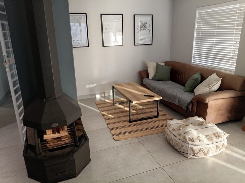 A bright living room featuring large format floor tiles, a modern freestanding fireplace, and venetian blinds, creating a comfortable and well-maintained living space.
