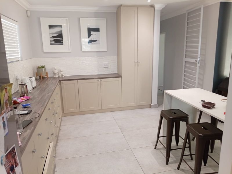 Modern kitchen featuring neutral-toned built-in cabinetry, wood-look laminate countertops, a textured tiled backsplash, and large format floor tiles.