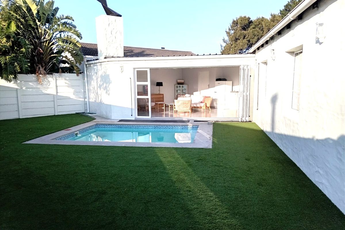 Rear garden area featuring a swimming pool, artificial lawn, and an outdoor fireplace, with bi-fold doors opening into the main living space.
