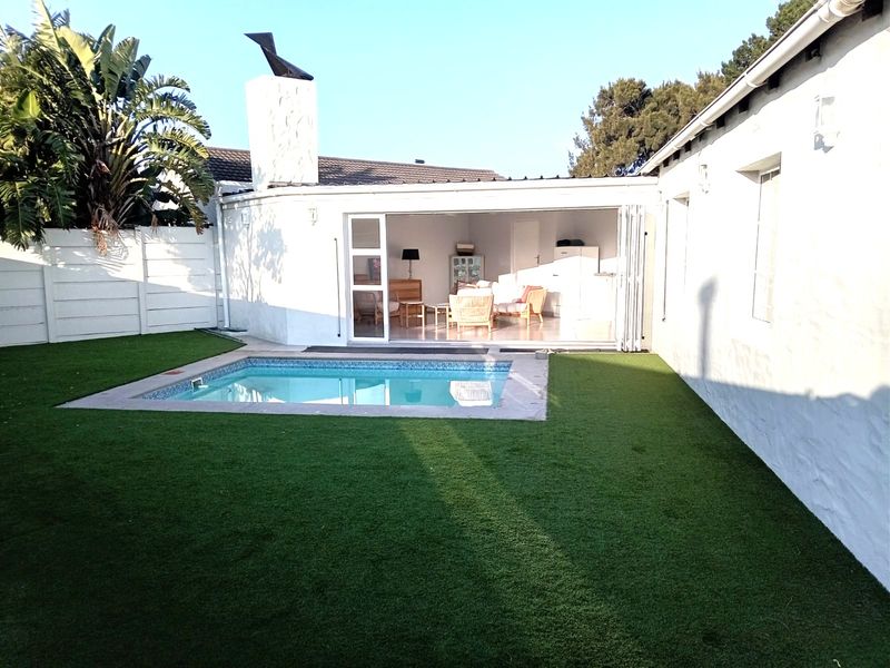 Rear garden area featuring a swimming pool, artificial lawn, and an outdoor fireplace, with bi-fold doors opening into the main living space.