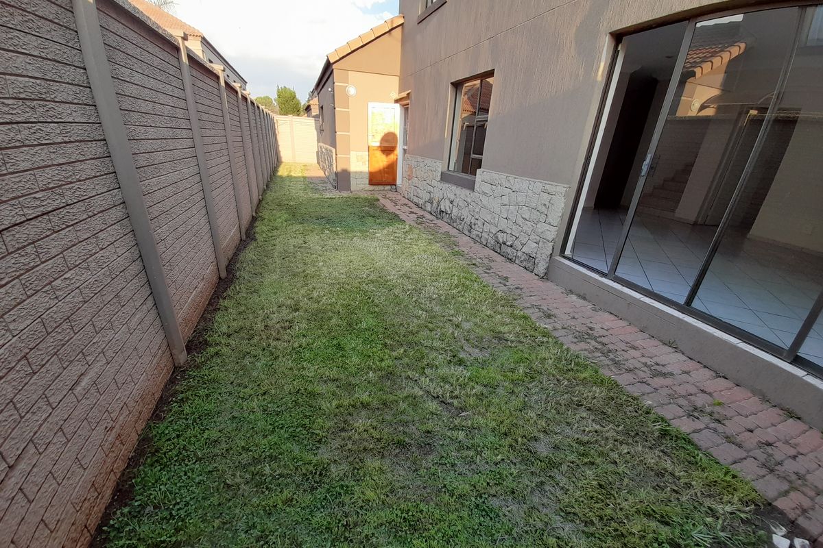 A rear exterior view of the townhouse featuring a small lawn, paved walkway, stone-clad wall accents, and sliding glass door access to the interior.