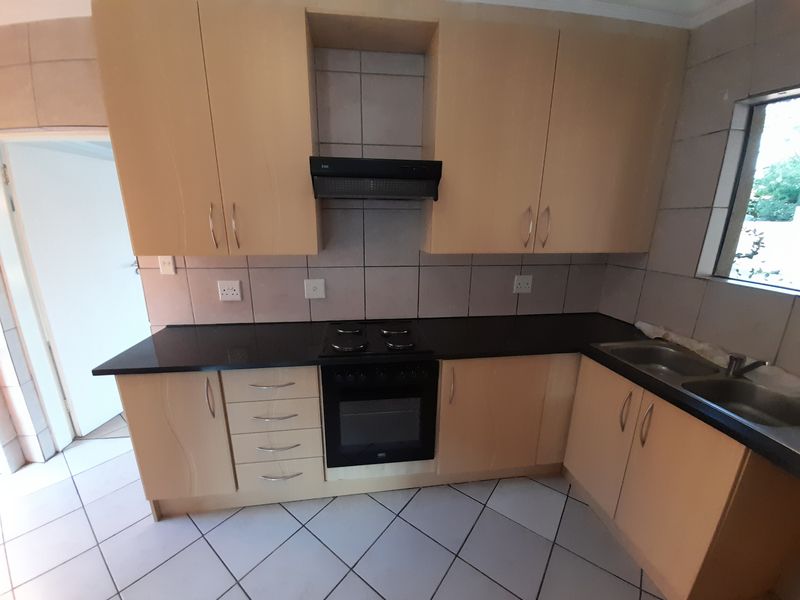 A functional kitchen featuring light wood-finish cabinetry, black granite countertops, a built-in oven with hob, and tiled flooring.