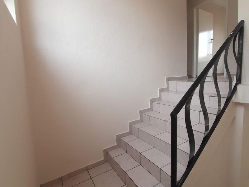 A clean, minimalist staircase featuring neutral floor tiles and a decorative black wrought iron balustrade leading to an upper landing.