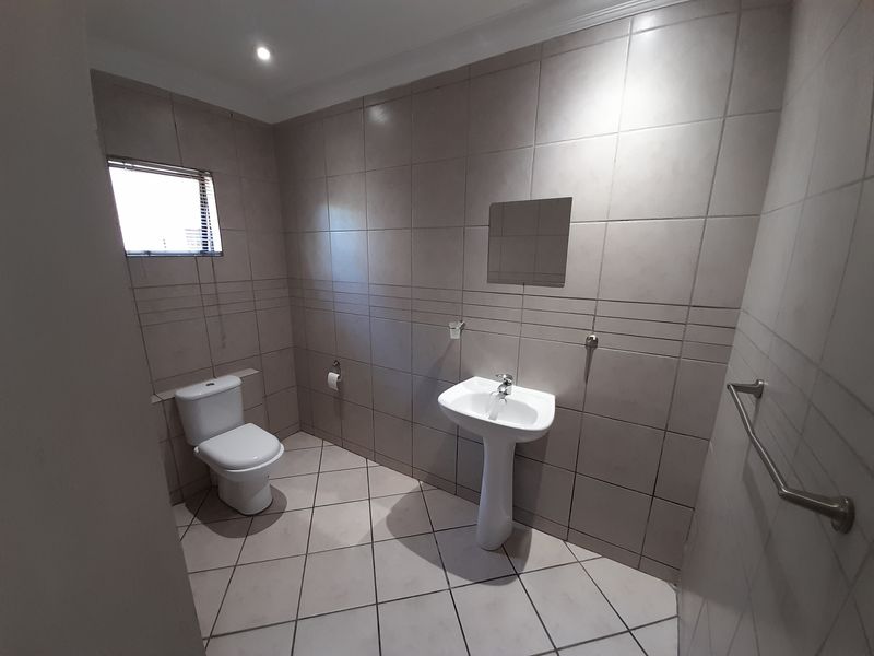 A clean and functional bathroom featuring a pedestal basin, toilet, and neutral floor-to-ceiling tiling.
