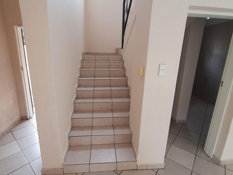 A bright, tiled hallway featuring a central staircase with a metal handrail, leading to upper levels in this townhouse.