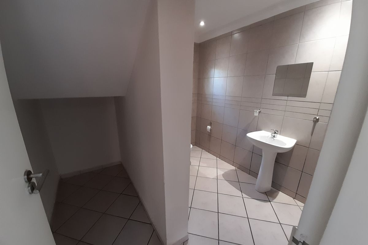 A clean, tiled guest bathroom featuring a pedestal basin and under-stair storage space.