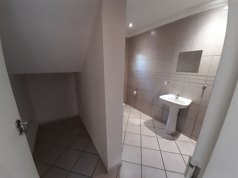 A clean, tiled guest bathroom featuring a pedestal basin and under-stair storage space.