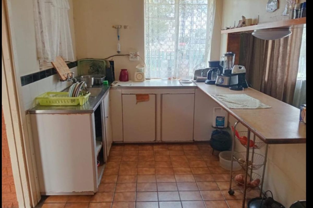 A compact, dated kitchen featuring tiled flooring, built-in cabinetry, and a stainless steel sink, offering potential for a modern renovation.