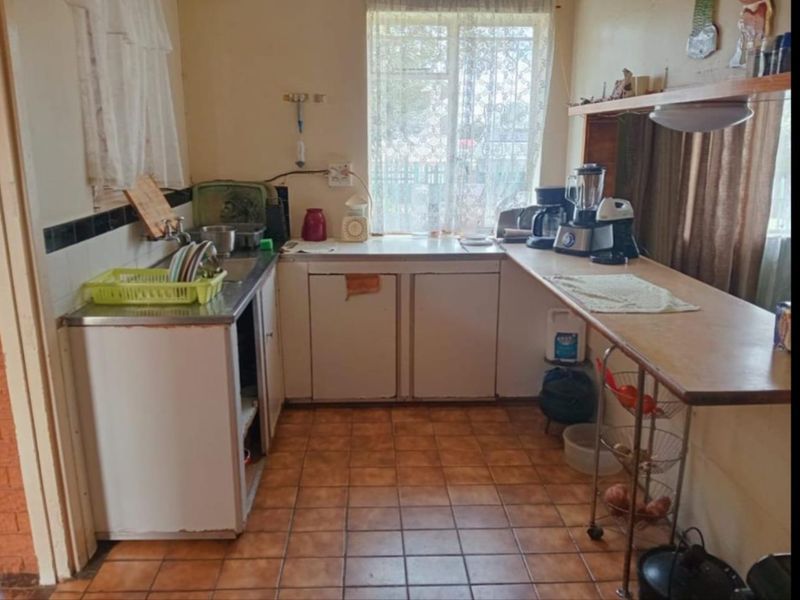 A compact, dated kitchen featuring tiled flooring, built-in cabinetry, and a stainless steel sink, offering potential for a modern renovation.