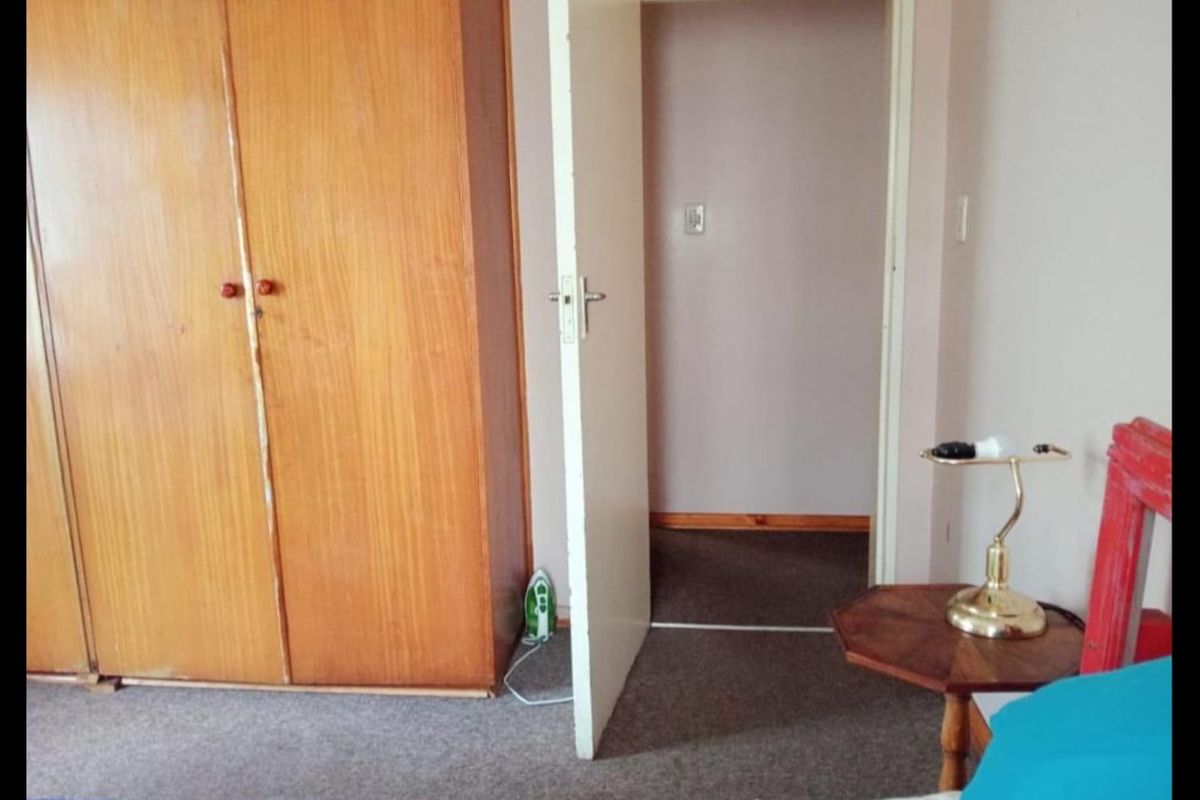 A bedroom featuring a built-in wooden wardrobe, carpeted flooring, and an internal doorway leading to an adjacent space.
