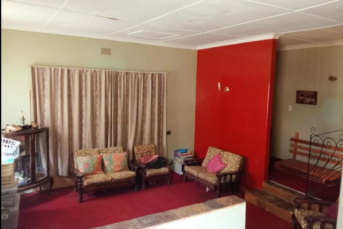 A living room featuring a red accent wall, tiled ceiling with visible water staining, and a stone-topped half wall partition.