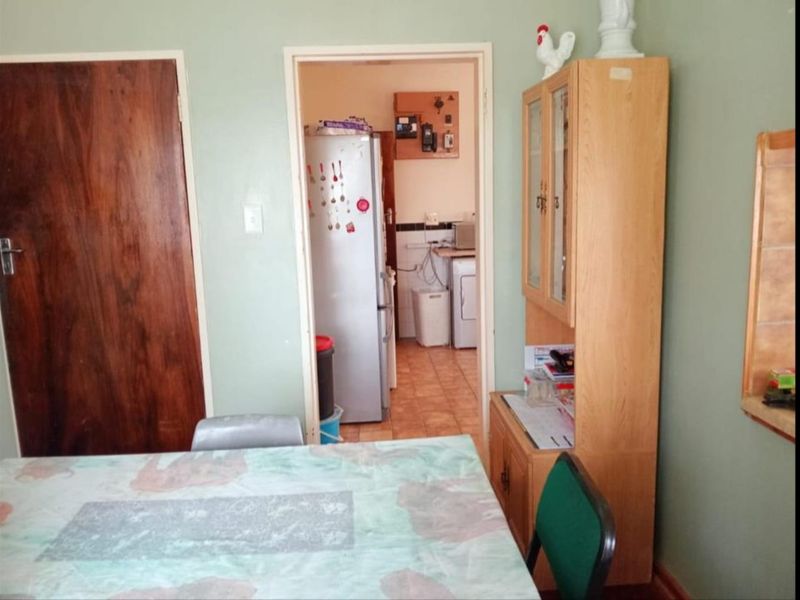 A dining area featuring tiled flooring and a wooden door, with a view into an adjacent utility or kitchen space.