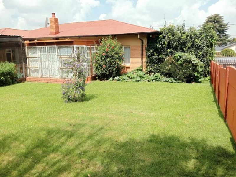 Rear view of the property featuring a spacious lawn, enclosed patio area, and brick chimney against a metal roof.