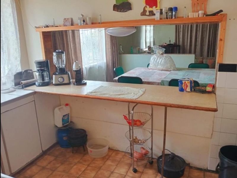 A dated kitchen area featuring a laminate breakfast bar, wall-mounted mirror, and tiled flooring, offering potential for a modern renovation.