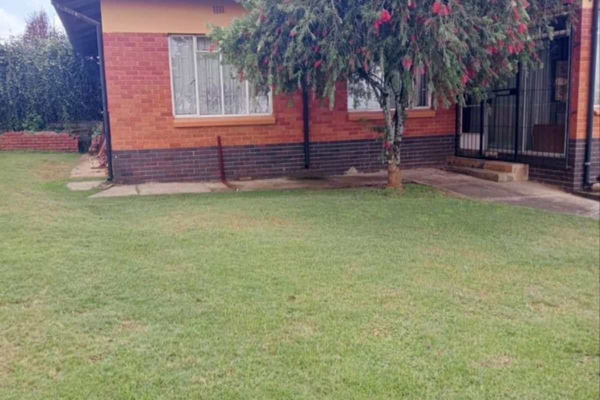 Rear view of a brick house featuring a metal roof, security gate, and a spacious lawn area.