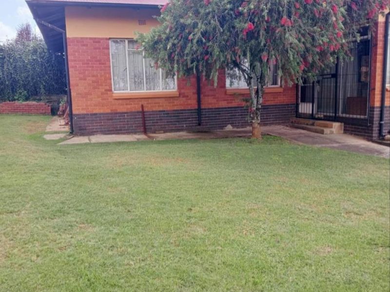Rear view of a brick house featuring a metal roof, security gate, and a spacious lawn area.