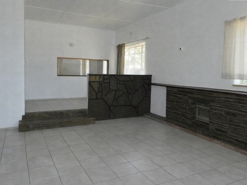 Spacious, empty living area featuring tiled flooring, a raised platform, and a prominent stone-clad fireplace and room divider.