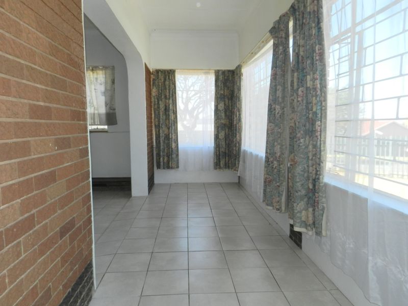 A sun-filled enclosed patio or sunroom featuring tiled flooring, exposed brick accents, and large windows with security bars.